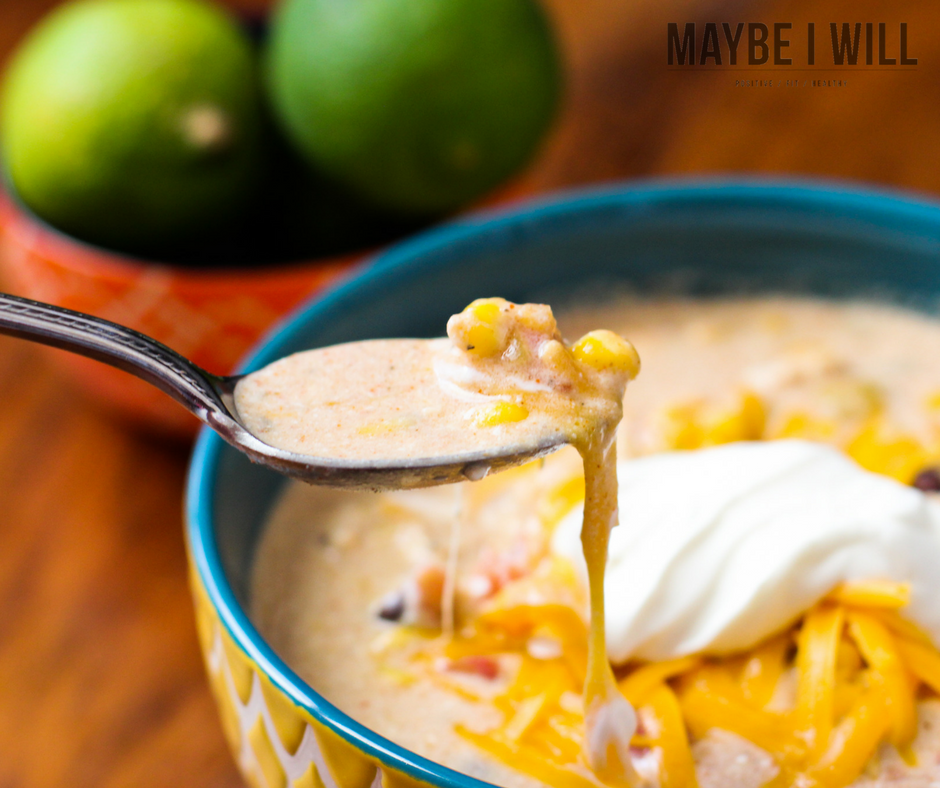 Close up of Crockpot Chicken Chili. Photo shows the chili served with melted shredded cheese and a dollop of sour cream. fresh limes are in the background 