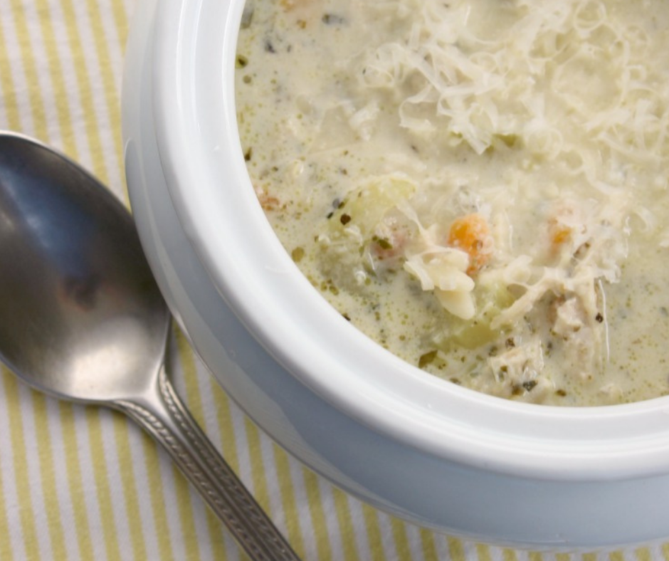 Close up of Hot Chicken Pesto Soup With Orzo over stripped yellow and white towel with a spoon off to the side.