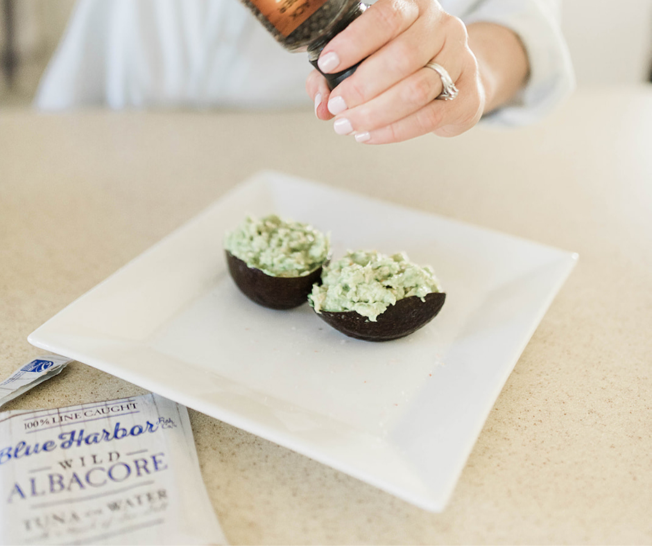 Open Avocado Halves with tuna and avocado mixture, woman is cracking fresh pepper over the top 