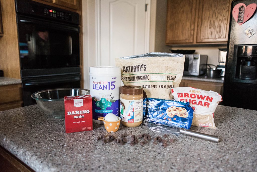 Photo of ingredients lined up that are needed to make a skillet cookie. coconut flour, peanut butter, chocolate chips, egg, protein powder, baking soda and brown sugar.