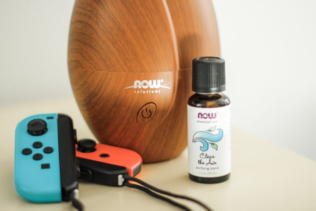Image of essential oil blend clear the air perfect for helping to deodorize "stinky teen" spaces. photo of bottle, game controllers, and a diffuser. 