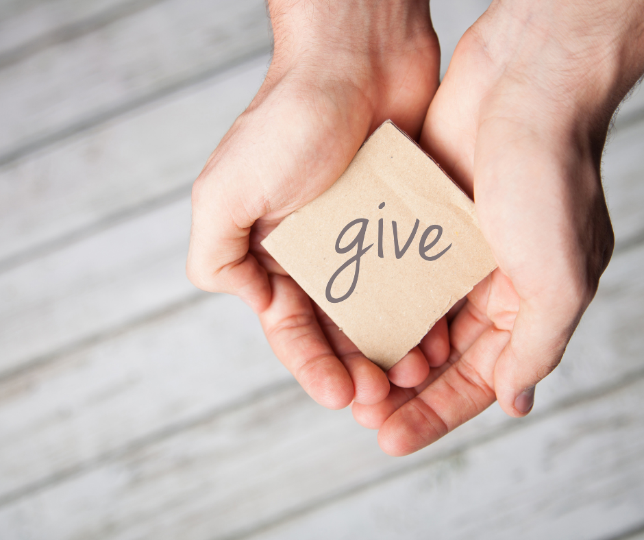 Photo of woman holding the word "give" on cardboard colored paper in her hands. 