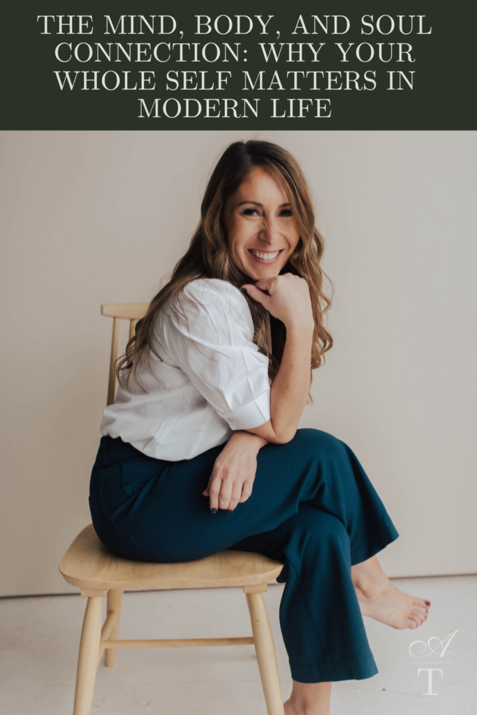 Photo of Andie sitting on a chair with her legs crossed leaning her head on her fist for a soft pose. She is discussing the mind, body, and soul connection