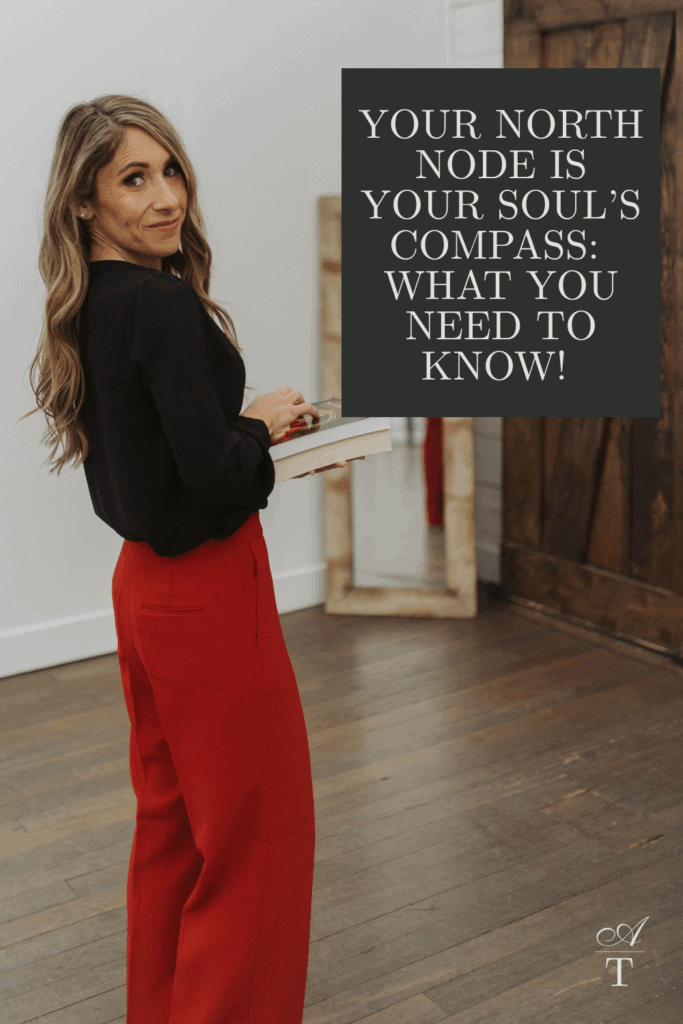 Andie is standing with some books at a side angle looking over her shoulder. She is wearing red dress pants and a black silky top. The words " Your North Node Is Your Soul’s Compass: What You Need To Know!" are written on the image. 