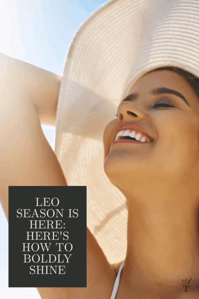 Photo of a woman in a big sunhat soaking in the sun with a big smile on her face, you can feel her joy. The words "Leo Season is Here, Here's How To Boldly Shine are written on the image. 