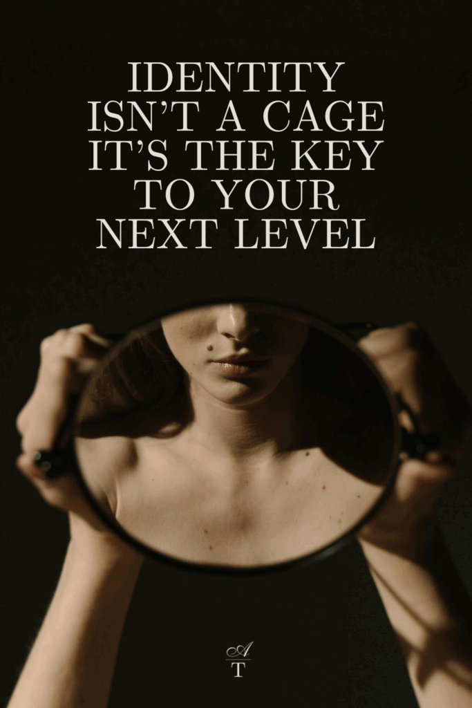 Image of woman holding a mirror you can only see the reflection and her hands holding the mirror. It has a dark and moody vibe. The wordds Identity isn't a cage, it's the key to your next level are transposed over the image.